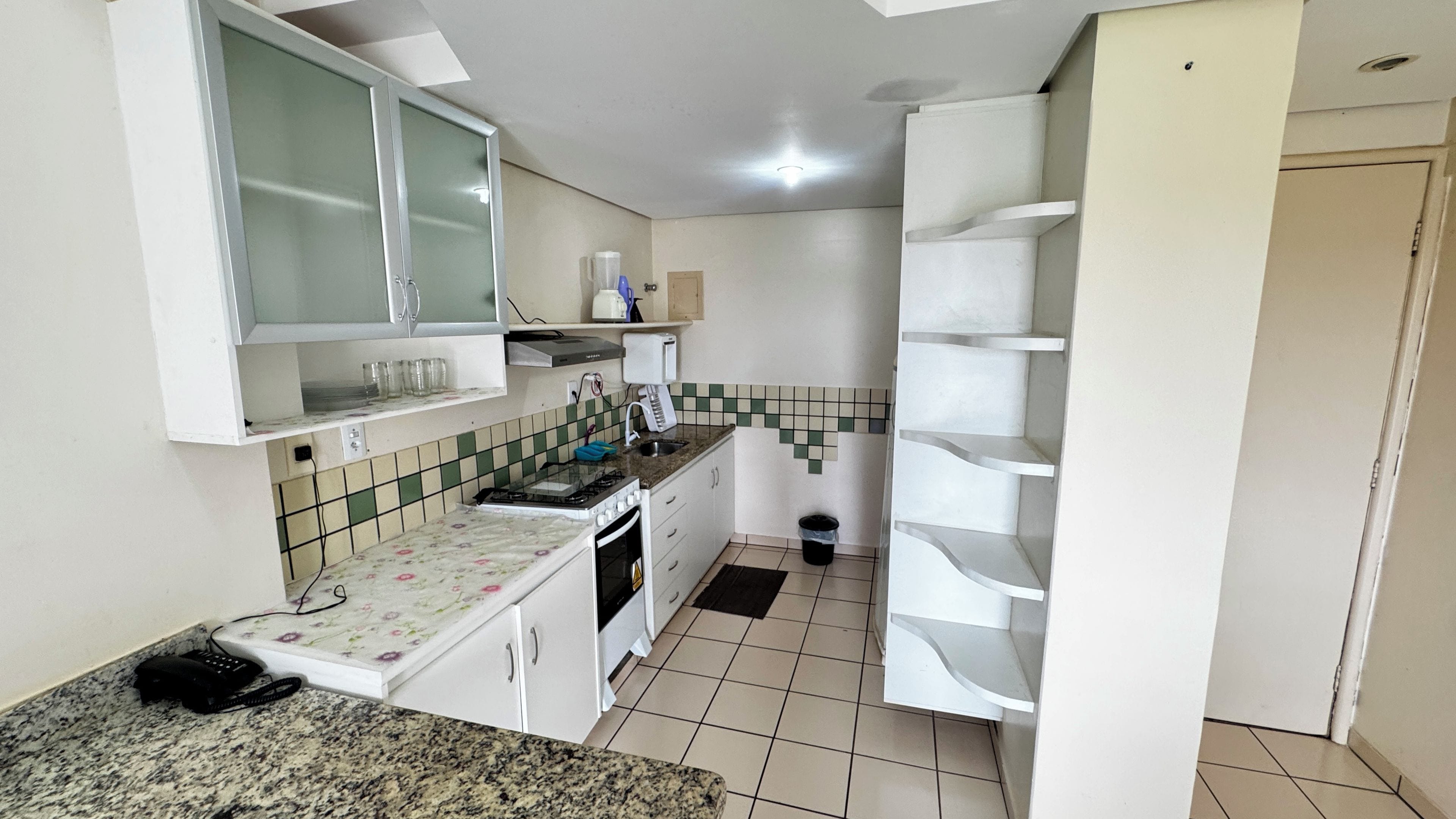 Une cuisine de taille réduite avec des meubles blancs, une cuisinière à gaz, un évier et un plan de travail.