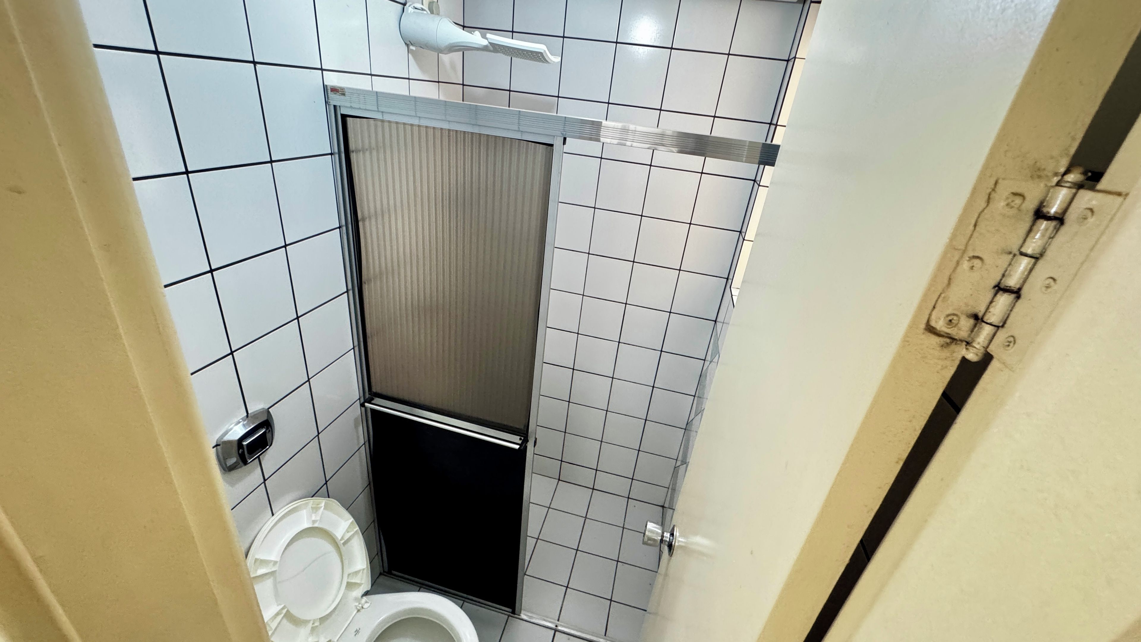 Um banheiro pequeno, com azulejos, incluindo vaso sanitário, box de chuveiro e porta-papel higiênico.