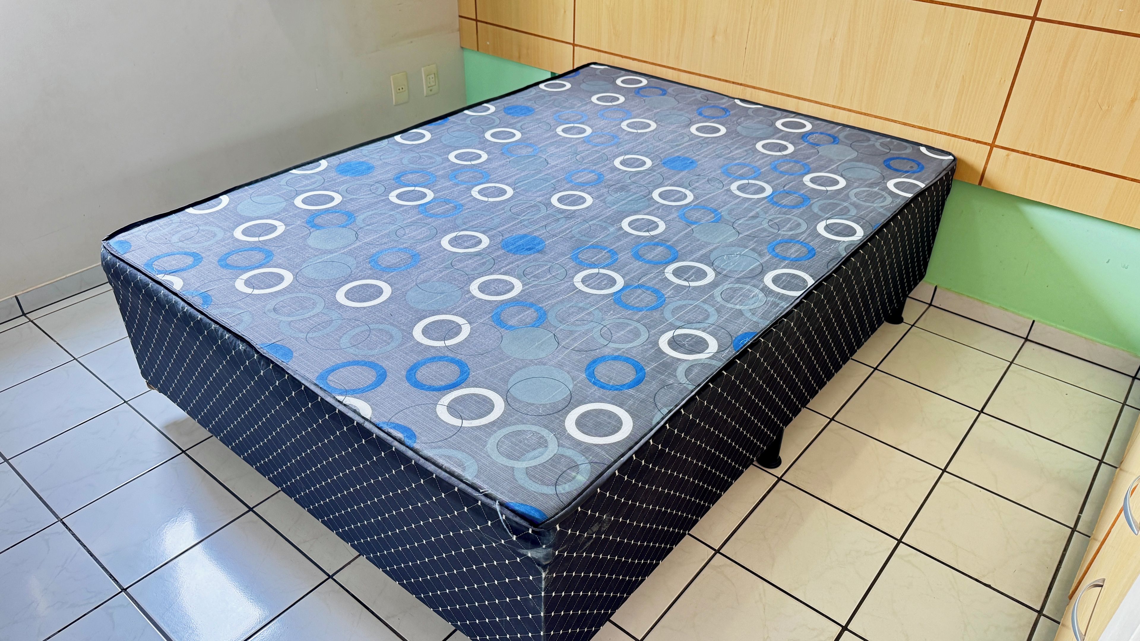 Een klein, vierkant tafeltje met een tafelkleed met patroon, een zwart gaas onderstel en een betegelde vloer.