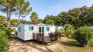 A single-story mobile home with a deck, surrounded by greenery and trees. - Mobile Home 'Location' with Shared Pool, Wi-Fi and Air Conditioning (Argelès-sur-Mer)