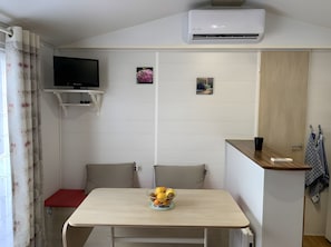 Habitació petita i neta amb un llit, televisió, aire condicionat fixat a la paret i una taula amb un plat de fruita.
