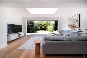 Sala de estar moderna com sofá, TV e vista para um jardim através de uma porta de vidro.