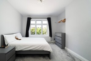 Quarto com cama, penteadeira, mesa de cabeceira e janela com cortinas.