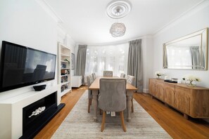 Ein modernes Wohnzimmer mit Fernseher, Esstisch mit Stühlen, Holzschrank und großem Spiegel.