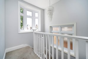 Quarto com corrimão branco, um lustre e janela com vista para um edifício.