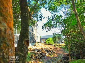 A rustic stone pathway leading to a modern building with a sloped roof, surrounded by lush greenery and trees. - Casas do Morgadio - Wine and Lodge (Açores)