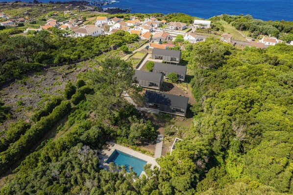 An aerial view of a residential area with houses, a swimming pool, and a coastline. - Casas do Morgadio - Wine and Lodge (Açores)