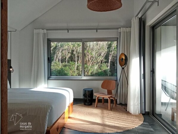 Un dormitorio moderno con un ventanal grande, una cama, una silla y una lámpara de pie.