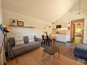 Una sala de estar moderna con un sofá, una mesita y un comedor con sillas. Se ve una cocina al fondo con un microondas y armarios.