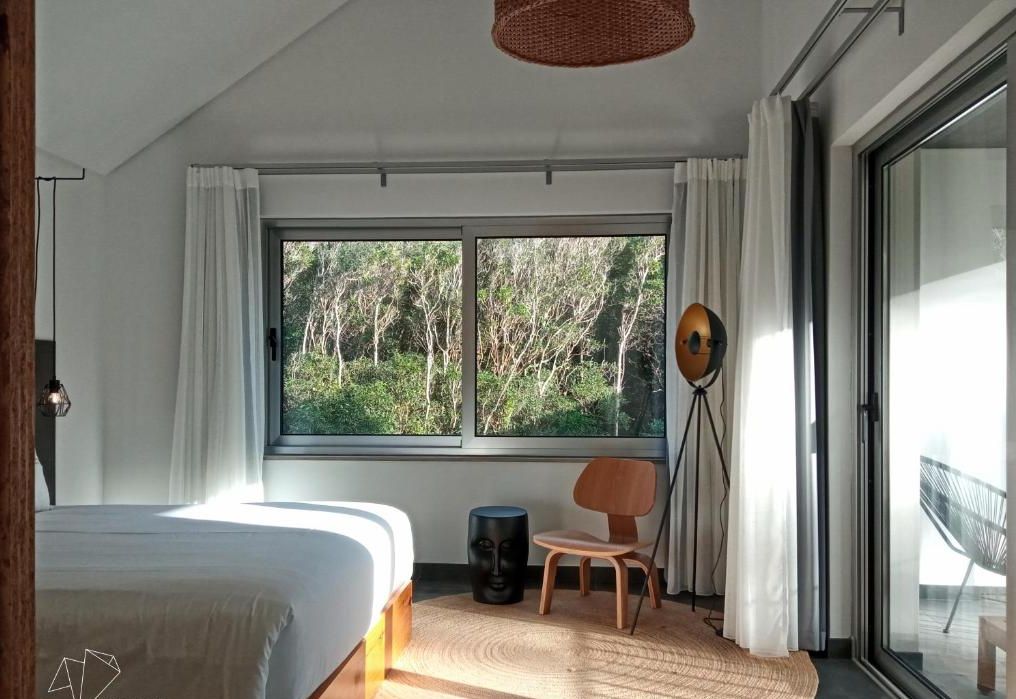 Un dormitorio moderno con un ventanal grande, una cama, una silla y una lámpara de pie.