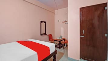 A bedroom with a bed, a wooden door, a small table with a chair, and a mirror on the wall.