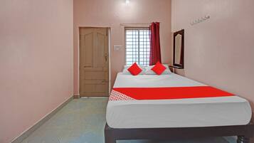 A bedroom with a bed, a door, a window with curtains, and a mirror on the wall.