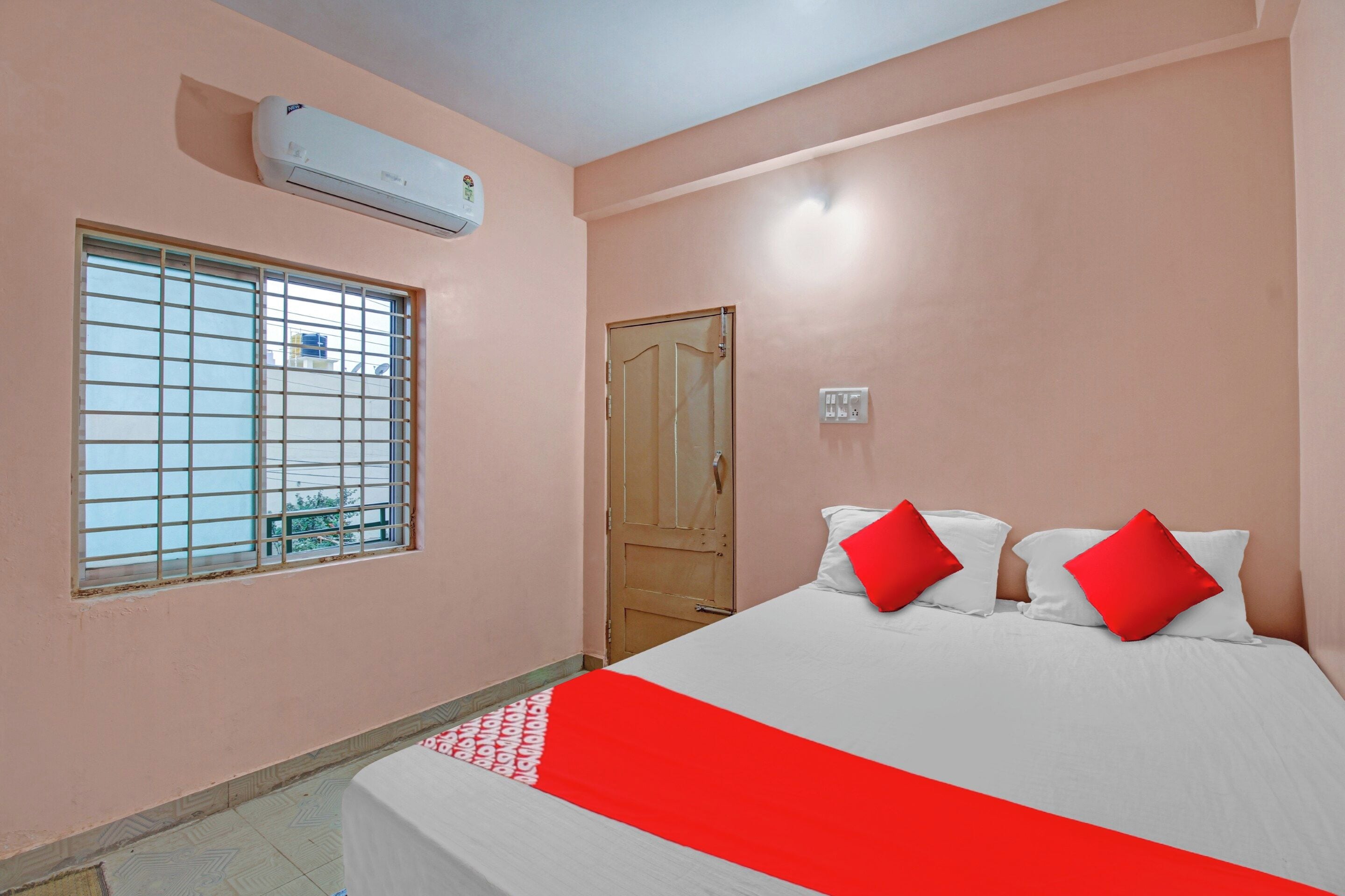 A bedroom with a bed, a window with bars, a door, and an air conditioning unit.