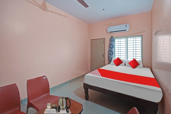 Una habitación de hotel con una cama, una silla, una mesa con hervidor y un aire acondicionado.