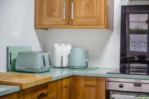 A kitchen with wooden cabinets, a stainless steel refrigerator, a coffee maker, and a kettle on a glass countertop.