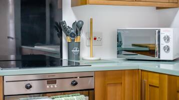 Une cuisine équipée d’un four à micro-ondes, d’un four en acier inoxydable et d’un ensemble d’ustensiles de cuisine rangés dans un porte-ustensiles.