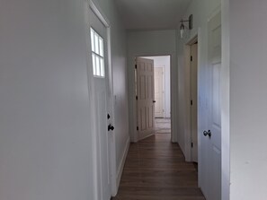 Un pasillo con puertas blancas, piso de madera y una lámpara en la pared.