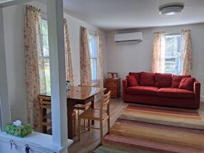 Una sala de estar con un sofá rojo, una mesa de comedor de madera, sillas y un tapete a rayas de colores.