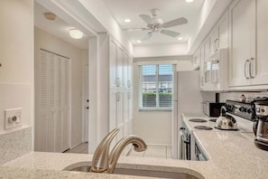 A kitchen with white cabinets, a stainless steel sink, a stove, and a ceiling fan. - Sunrise Cove 103: Ground Floor Waterfront Condo on Siesta Key w/ Sleeper Sofa (Sarasota)