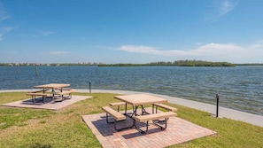 Un espace de pique-nique aménagé au bord du lac, avec des tables et des bancs installés sur une plateforme en briques.