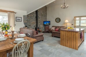 Ein gemütlicher Wohnbereich mit Steinwand, Kamin, Fernseher und einem für eine Mahlzeit gedecktem Esstisch.