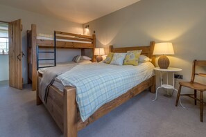 Ein Schlafzimmer mit Etagenbett, einem Einzelbett, einem Nachttisch mit Lampe und einem Sessel.