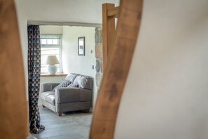 A room with a grey sofa, patterned curtains, a lamp, and a stone wall. - Large 4 Bedroom Holiday Cottage on the Llŷn Peninsula | Deri-Sarn (Pwllheli)