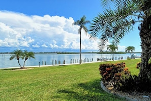 A waterfront property with a grassy lawn, palm trees, and a view of the water. - Sunrise Cove 108: Ground floor Waterfront Condo on Siesta Key w/ Sleeper Sofa (Sarasota)