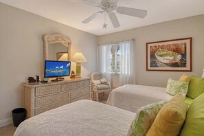 Een hotelkamer met twee bedden, een televisie, een dressoir, een stoel en een plafondventilator.