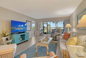 A living room with a television, sofa, chairs, and a view of the outdoors. - Sunrise Cove 108: Ground floor Waterfront Condo on Siesta Key w/ Sleeper Sofa (Sarasota)