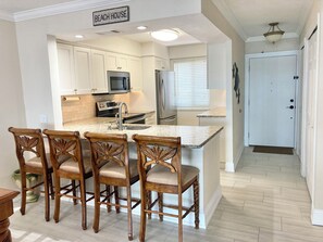A kitchen with white cabinets, a granite countertop, and a sign reading 'BEACH HOUSE'. - Sunrise Cove 110: Ground Floor Waterfront Condo on Siesta Key w/ Washer/Dryer (Sarasota)