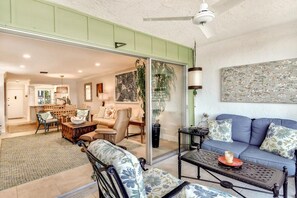 Ein Wohnzimmer mit einer Couch, Sesseln, einem Couchtisch und einer Schiebetür zu einem weiteren Raum.