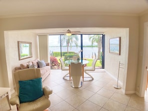 A room with a sofa, a dining table with chairs, a ceiling fan, and a view of a body of water. - Sunrise Cove 126: Remodeled Waterfront Condo on Siesta Key w/ Sleeper Sofa (Sarasota)