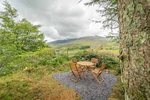 An outdoor seating area with a table and chairs, surrounded by natural landscape and a tree. - Two Bedroom Holiday Cottage At The Foot Of Yr Wyddfa (Snowdon) | Clogwyn-Bach (Rhyd Ddu)