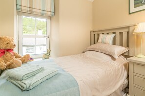 A bedroom with a bed, a bedside lamp, a teddy bear, and a window with a view of greenery. - Two Bedroom Holiday Cottage At The Foot Of Yr Wyddfa (Snowdon) | Clogwyn-Bach (Rhyd Ddu)