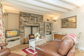 Ein gemütliches Wohnzimmer mit Kamin aus Stein, einem Fernseher, einem Bücherregal und Ledermöbeln.