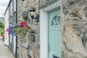 Ein Steinhaus mit einer grünen Tür, einem hängenden Blumenkorb und einer schwarzen Wandleuchte.