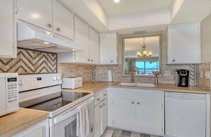 A modern kitchen with white cabinetry, a built-in oven, a microwave, and a coffee maker. - Sunrise Cove 201: Waterfront Condo on Siesta Key with Heated Lap Pool (Sarasota)
