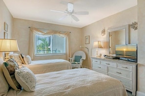 A hotel room with two beds, a ceiling fan, a television, and a window with curtains. - Sunrise Cove 201: Waterfront Condo on Siesta Key with Heated Lap Pool (Sarasota)