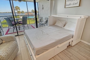 A bedroom with a bed, a chair, a small table, and a view of the sea. - Sunrise Cove 203: Remodeled Waterfront Condo on Siesta Key w/ Sleeper Sofa (Sarasota)