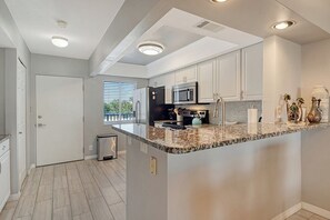 A modern kitchen with granite countertops, stainless steel appliances, and white cabinetry. - Sunrise Cove 203: Remodeled Waterfront Condo on Siesta Key w/ Sleeper Sofa (Sarasota)