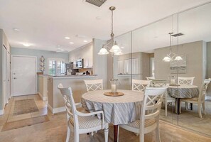 A dining area with a round table, white chairs, and a chandelier. - Sunrise Cove 227: Waterfront Vacation Condo on Siesta Key with Sleeper Sofa (Sarasota)