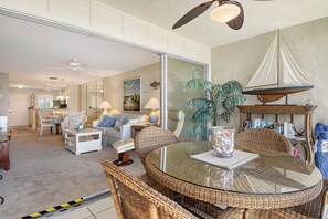 A spacious living area with a round glass table, wicker furniture, and a sailboat decoration. - Sunrise Cove 227: Waterfront Vacation Condo on Siesta Key with Sleeper Sofa (Sarasota)