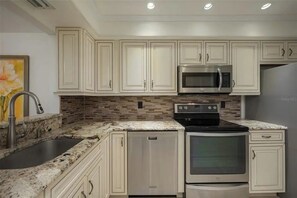 A kitchen with white cabinetry, a stainless steel microwave, an oven, and a dishwasher. - Sunrise Cove 228: Waterfront Vacation Condo on Siesta Key with Murphy Bed (Sarasota)
