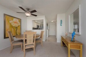 A dining area with a round table and chairs, a ceiling fan, a painting on the wall, and a console table with a mirror and decorative items. - Sunrise Cove 228: Waterfront Vacation Condo on Siesta Key with Murphy Bed (Sarasota)