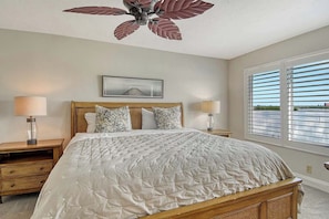 A bedroom with a large bed, two bedside tables, a ceiling fan, a window with blinds, and a framed picture on the wall. - Sunrise Cove 230: Remodeled Waterfront Condo on Siesta Key w/ Sleeper Sofa (Sarasota)