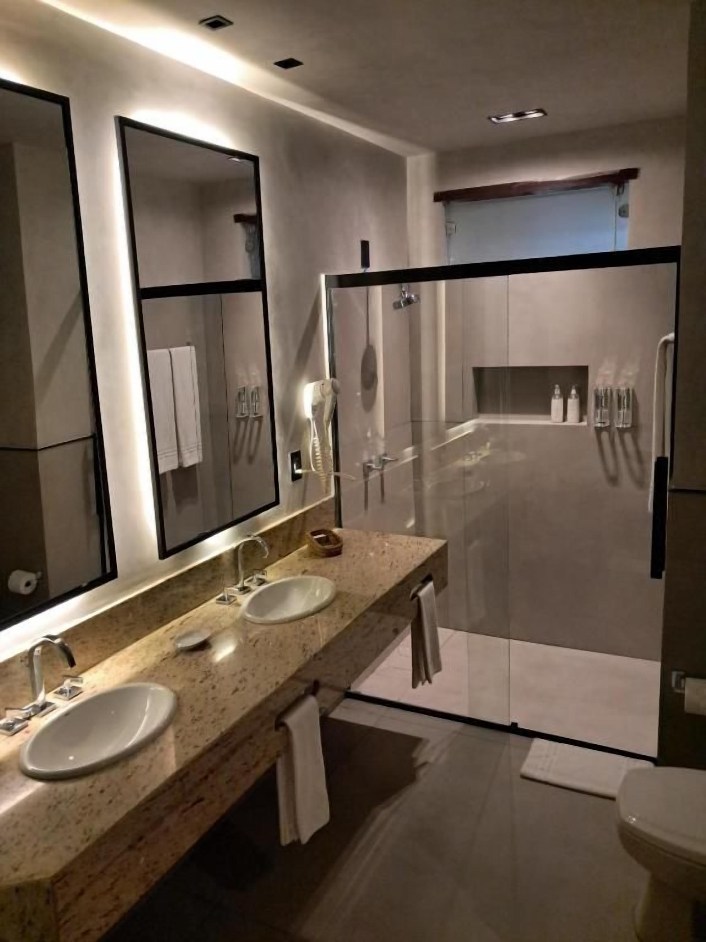 A modern bathroom with a double sink vanity, a large mirror, a shower enclosure, and a toilet.