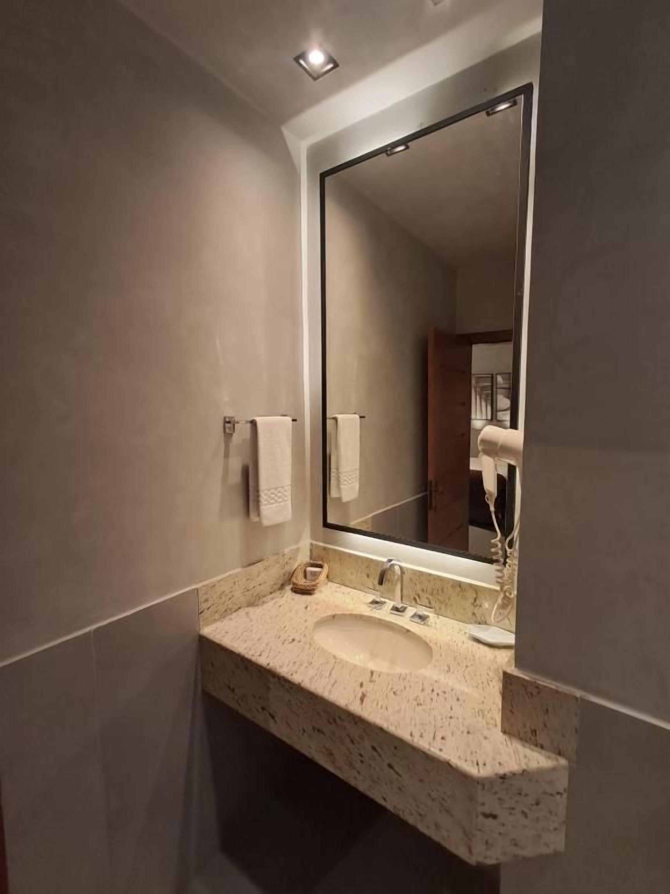 Un baño con lavamanos de mármol, un espejo grande y un perchero para toallas.