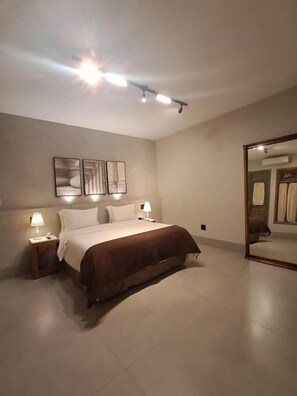 Un dormitorio con cama, lámparas de noche, una lámpara de techo y un espejo grande.