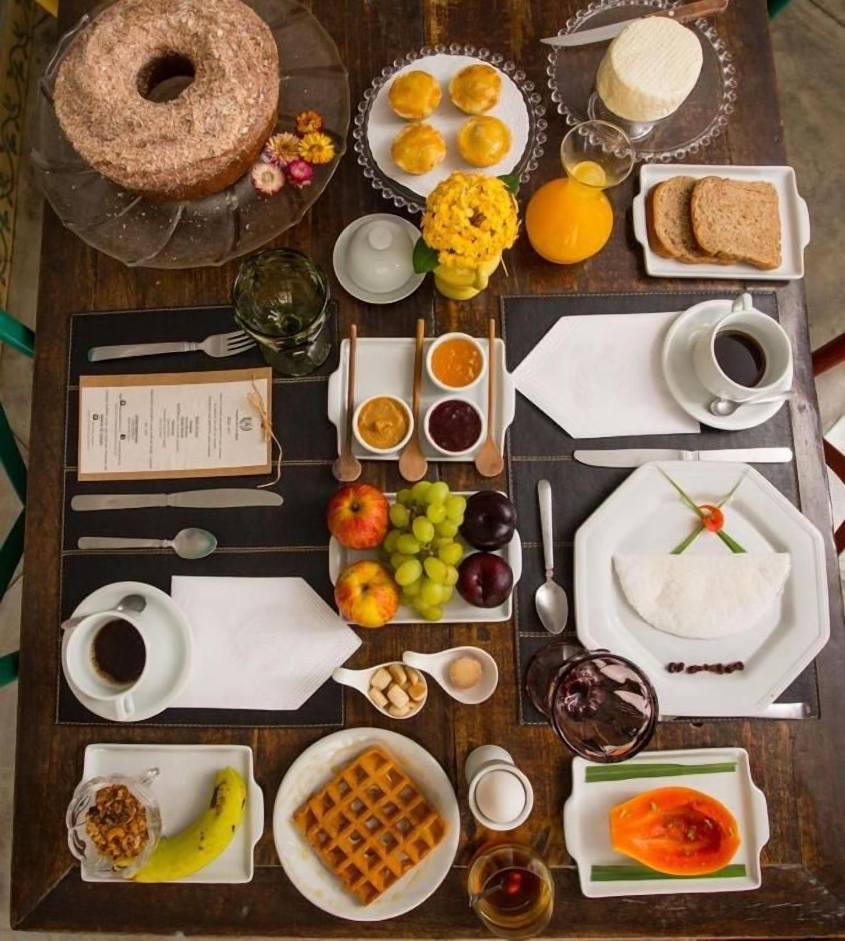 A breakfast buffet with various food items and utensils laid out on a wooden table.